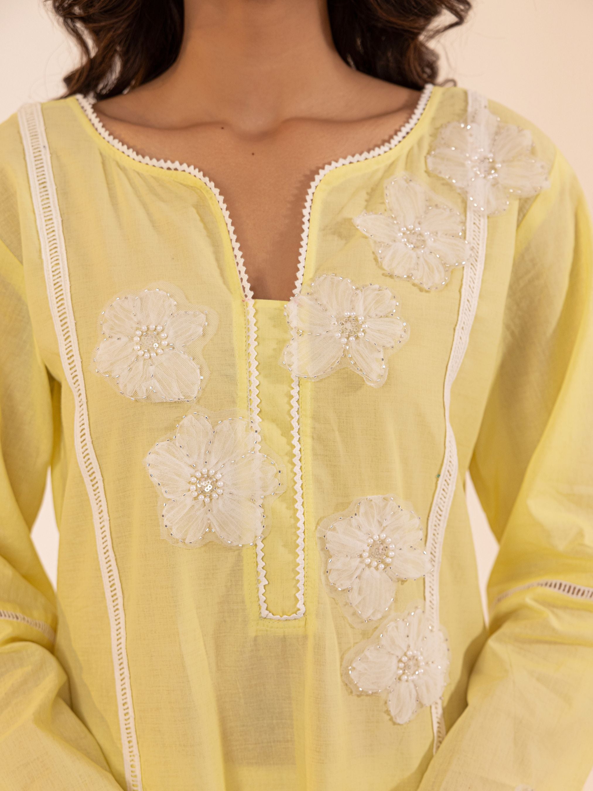 Yellow top with white floral embroidery on a plain background