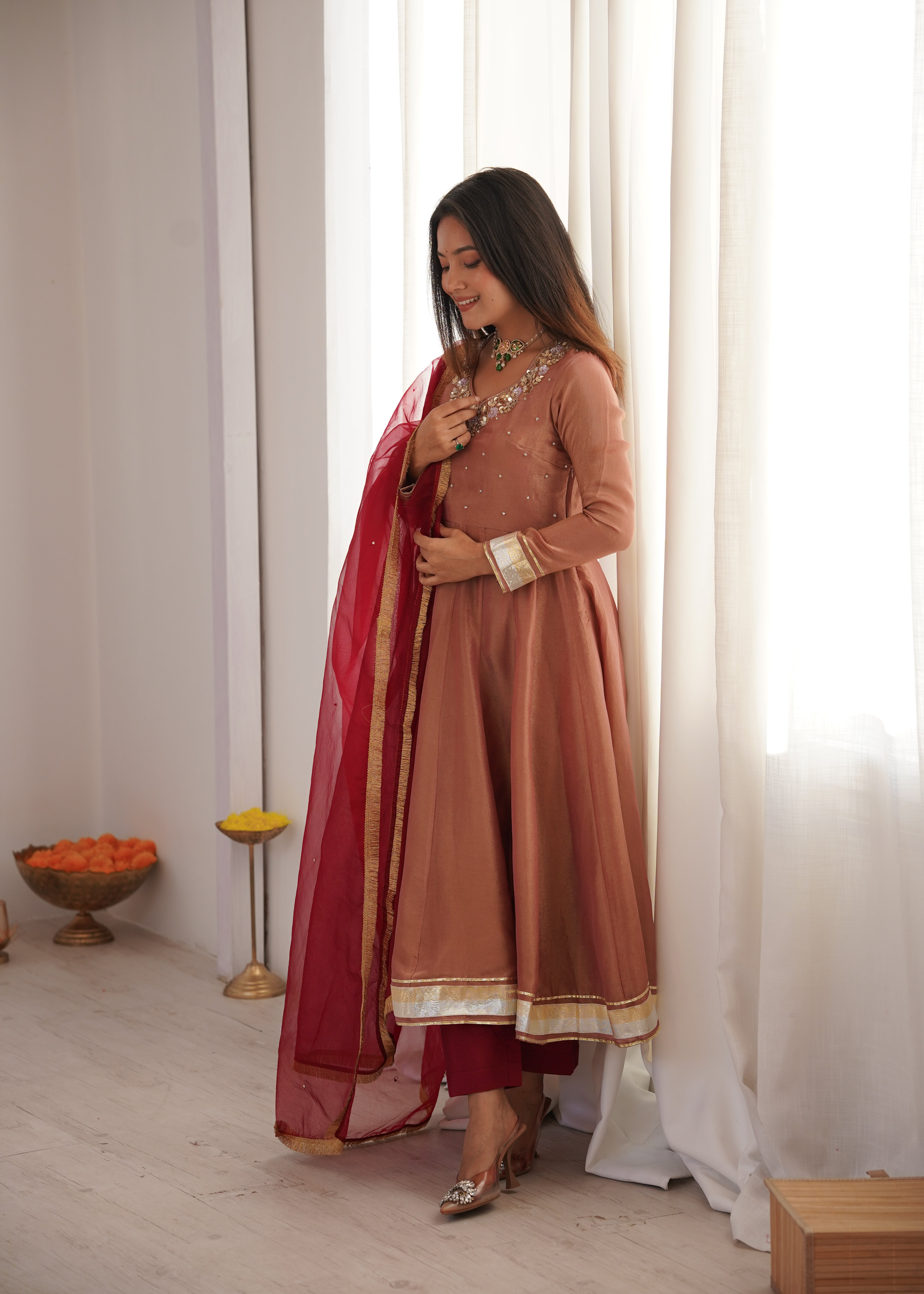 Woman in a traditional outfit standing in a room with white curtains and decorative items.